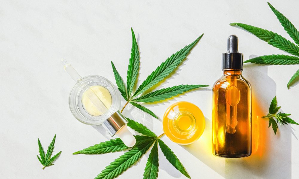 Glass brown bottle with cannabis oil with label and hemp leaves on a marble background. Copy space.